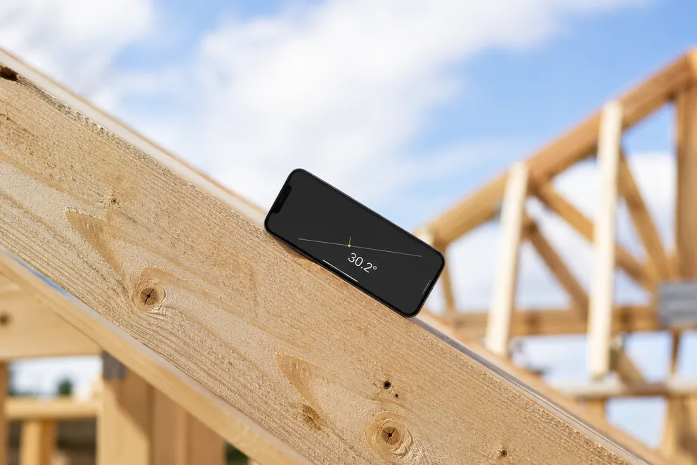 A phone held against a pitched roofline measuring the slope angle in degrees